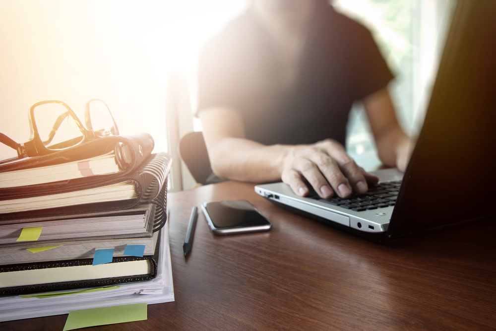 designer hand working with  digital tablet and laptop and notebook stack and eye glass on wooden desk in office